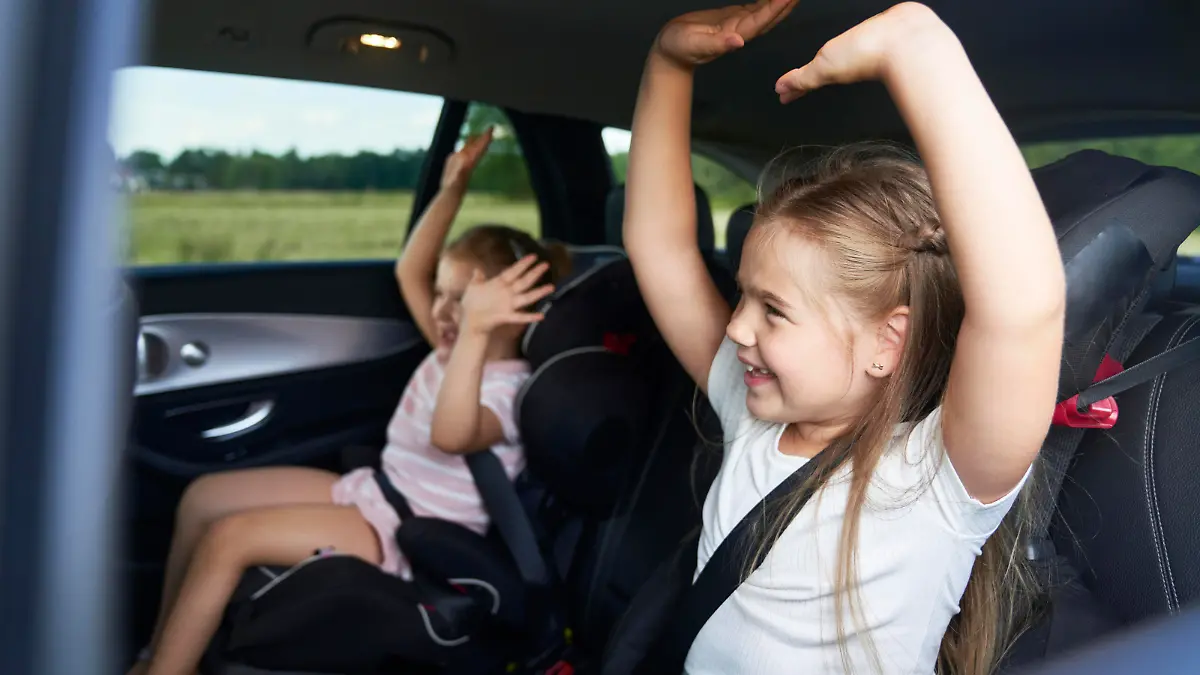 Two caucasian female children riding in the car in the back seat and dancing