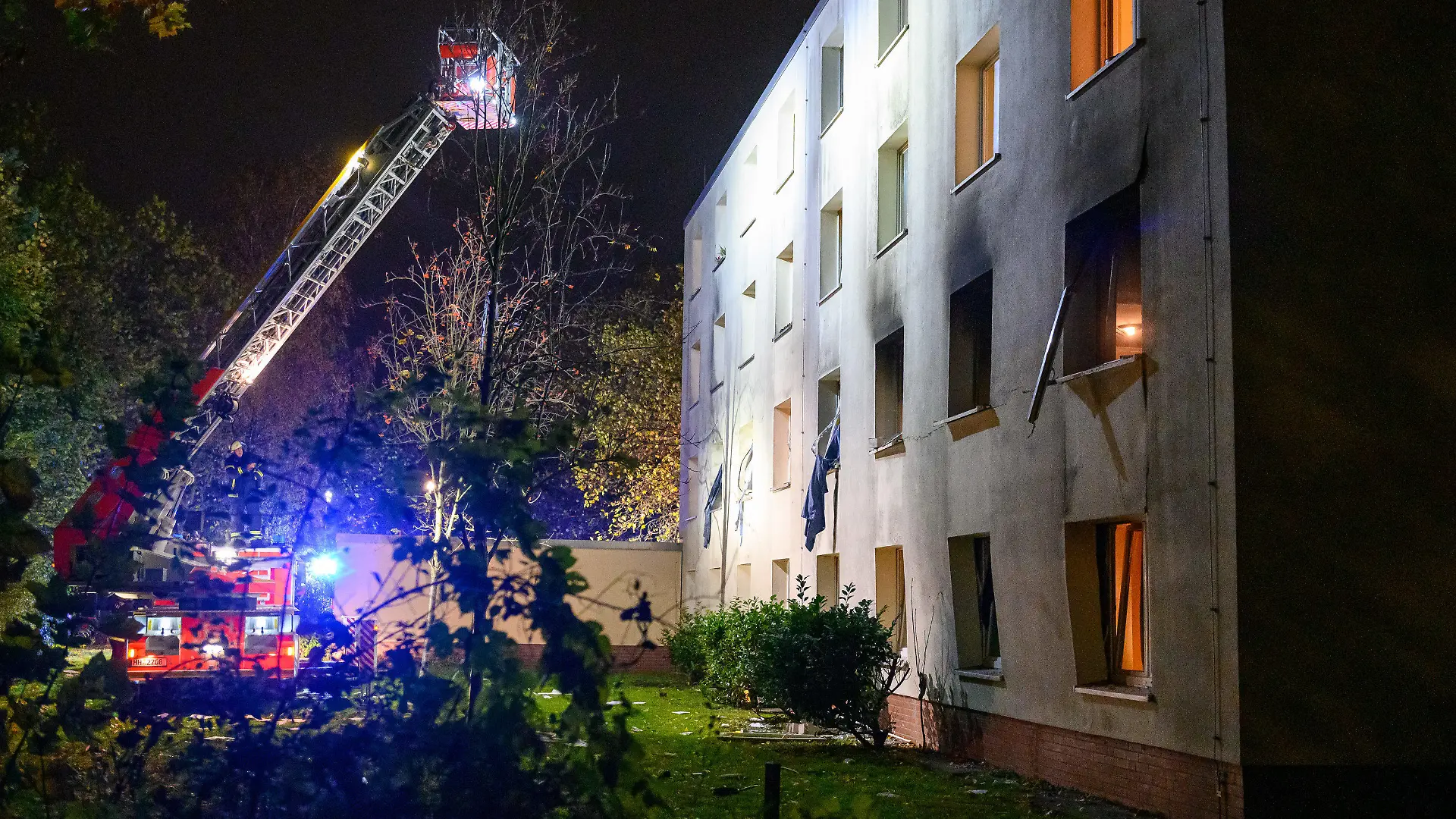10.11.2022, Hamburg: Eine Drehleiter der Feuerwehr beleuchtet die verrußte und beschädigte Fassade des Gebäudes. Bei einer Explosion in einem Männerwohnheim für Bedürftige in Hamburg-Stellingen ist ein Mann am Donnerstagabend lebensgefährlich verletzt worden. Foto: Jonas Walzberg/dpa +++ dpa-Bildfunk +++