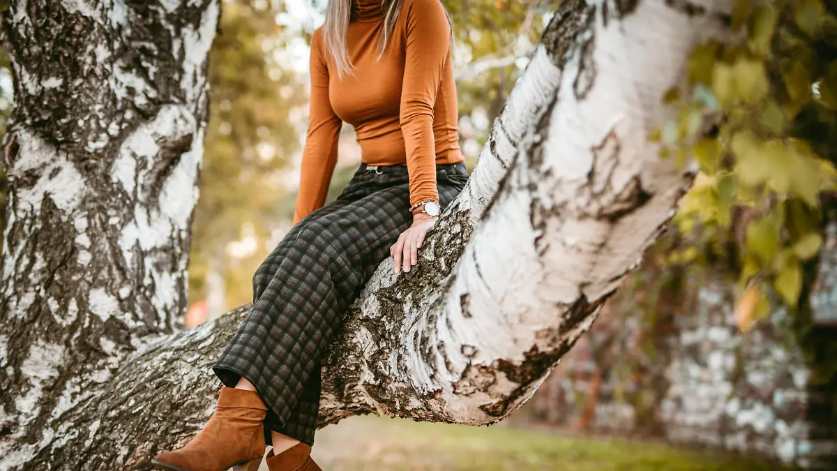 Young woman enjoys sunny autumn day in park, sitting on tree