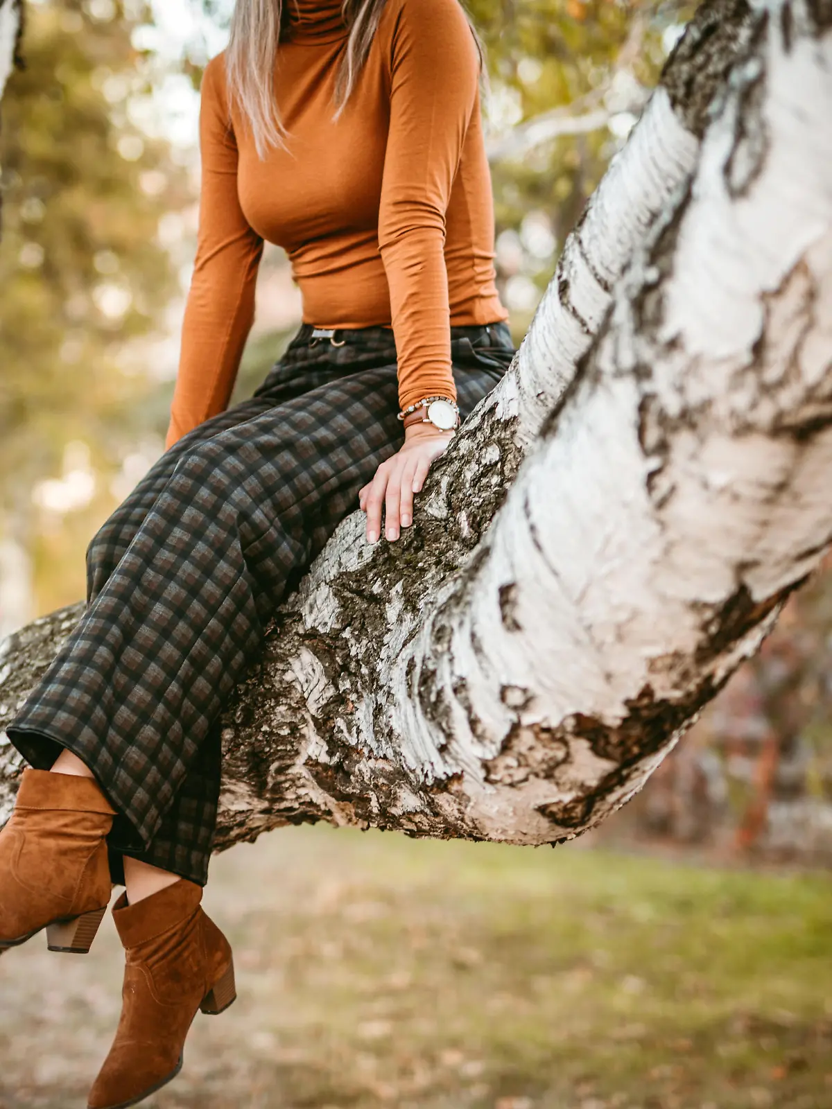 Young woman enjoys sunny autumn day in park, sitting on tree