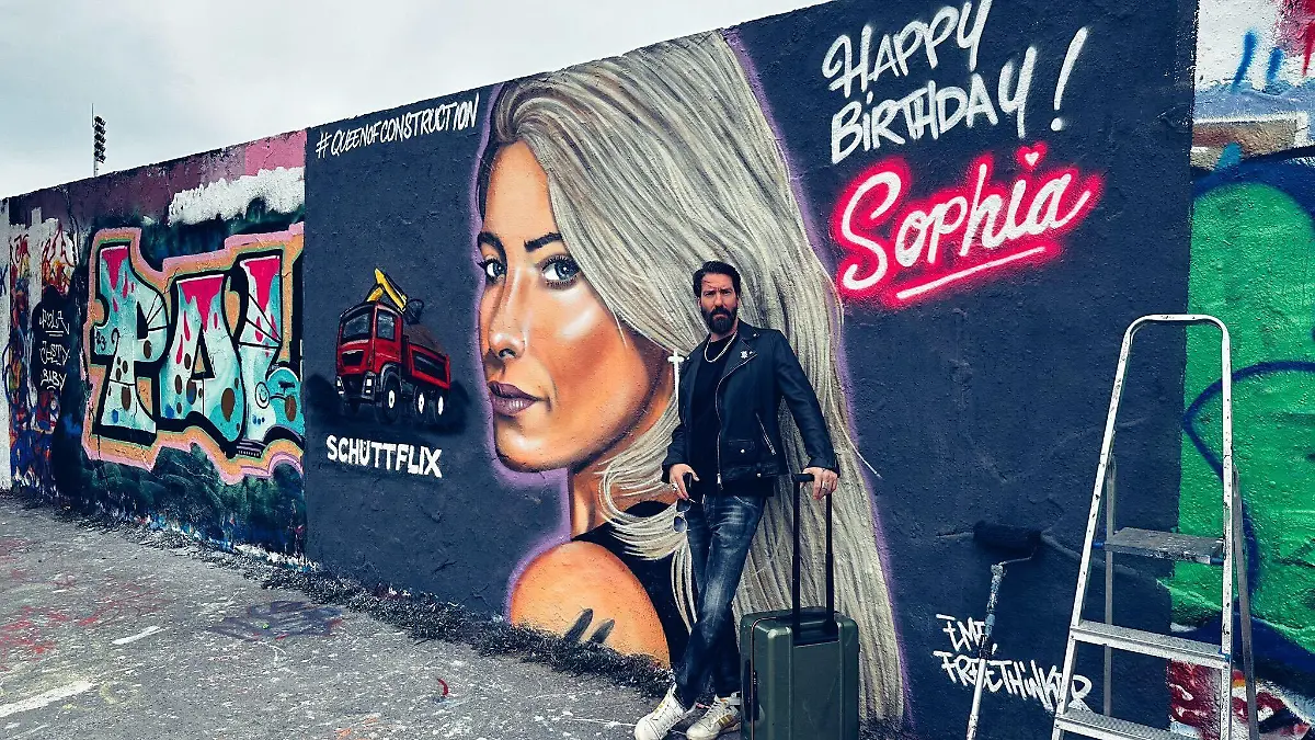Alec Voelkel vor einem Graffiti von Sophia Thomallas Gesicht.