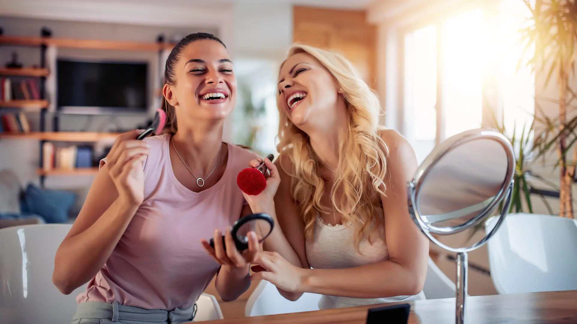 Two happy girls applying make up at home,having fun together.