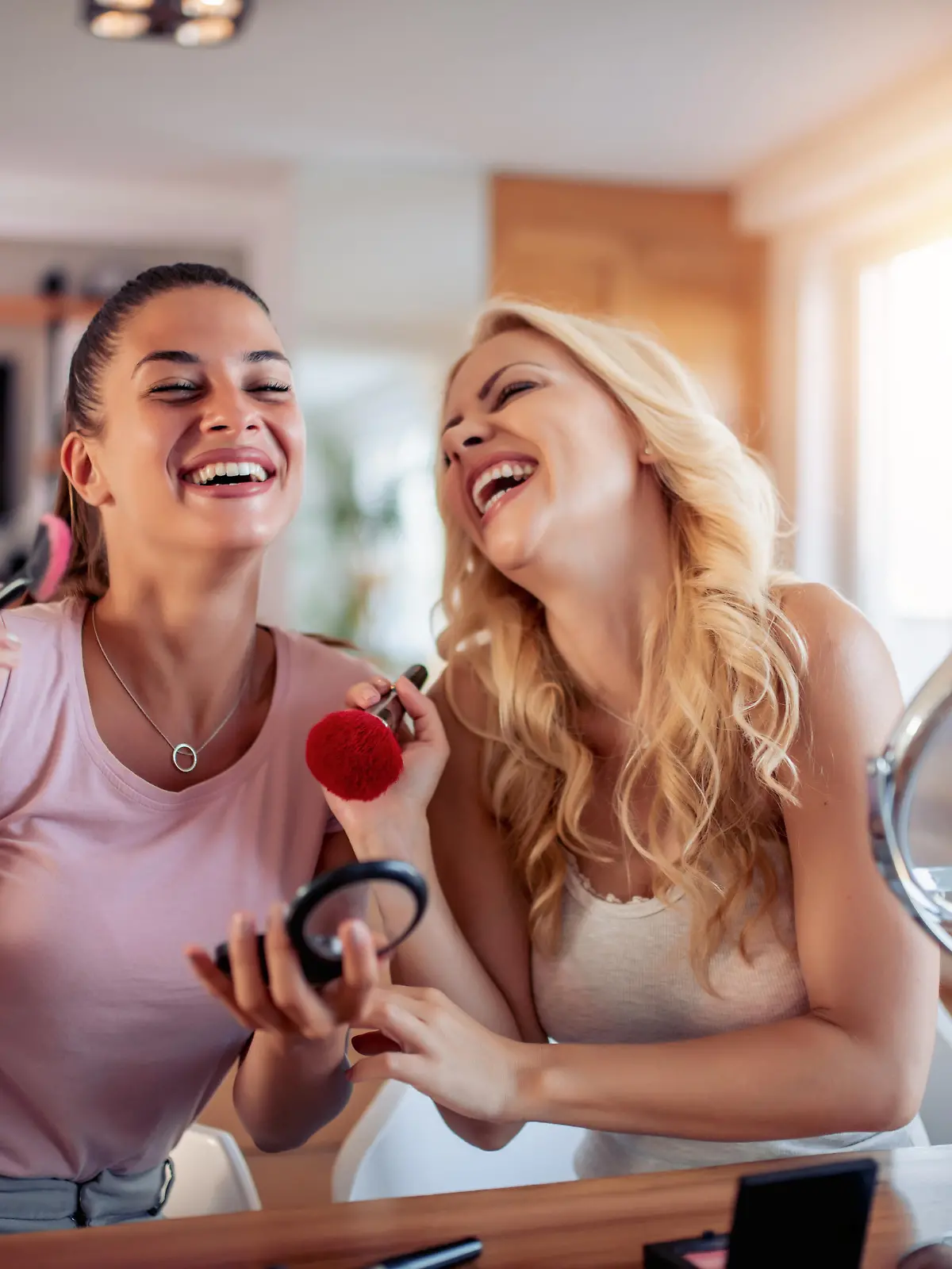 Two happy girls applying make up at home,having fun together.
