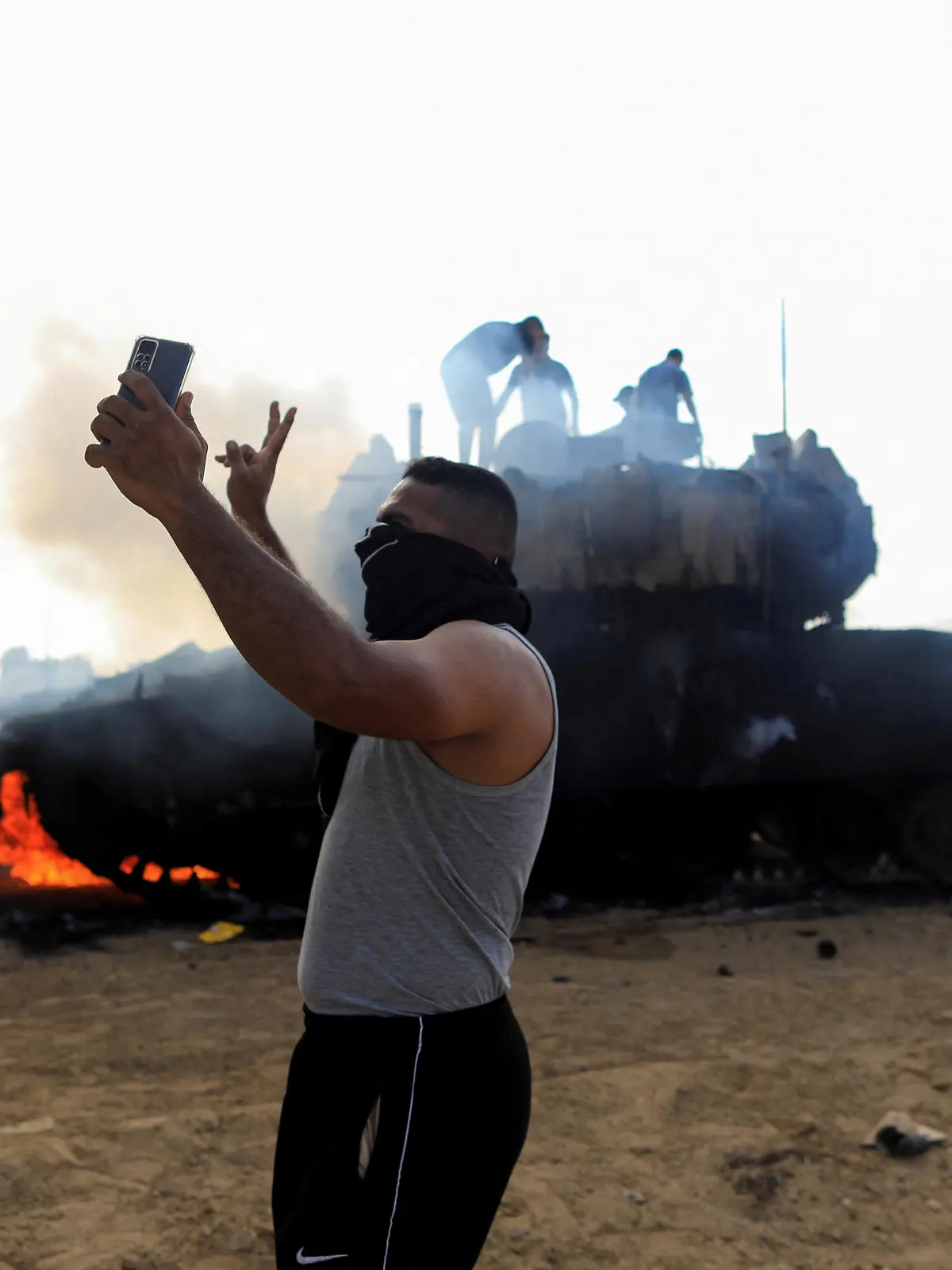 A Palestinian man takes a selfie in front of a burning Israeli military vehicle after it was hit by Palestinian gunmen who infiltrated areas of southern Israel, at the Israeli side of Israel-Gaza border, October 7, 2023. REUTERS/Yasser Qudih       NO RESALES. NO ARCHIVES.