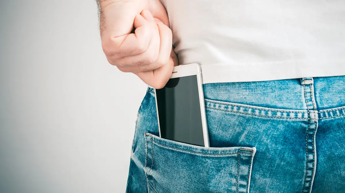 A Male Hand Grabbing A Smartphone In The Left Back Pocket Of A Jeans Trouser