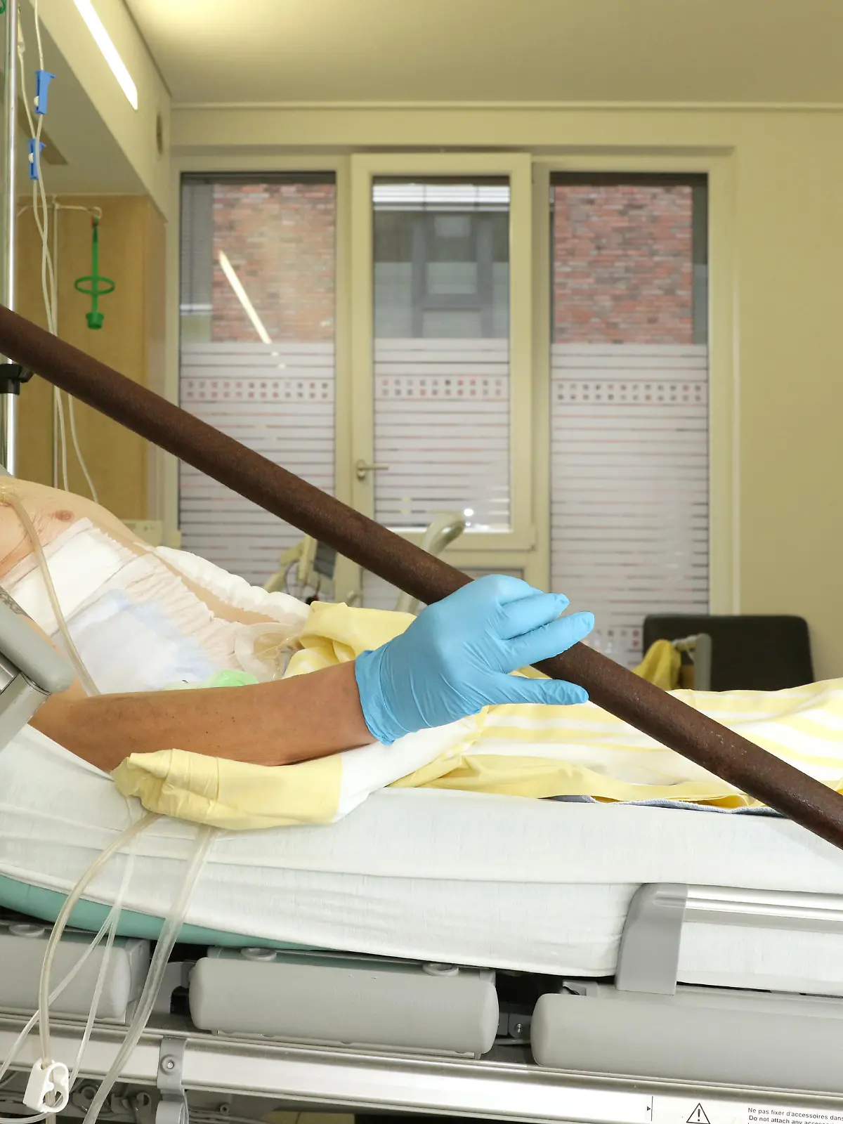 Ein Mann liegt in einem Krankenhausbett, er hält eine Stange in der Hand.
