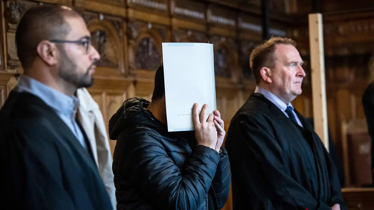 10.11.2022, Bremen: Der Angeklagte steht vor Prozessbeginn mit seinen Anwälten Manar Taleb (l) und Thomas Domanski (r) im Gerichtssaal. Nach der Gewalttat an einem Bremerhavener Gymnasium im Mai 2022 muss sich ein ehemaliger Schüler vor dem Landgericht Bremen wegen versuchten Mordes verantworten. Die Staatsanwaltschaft wirft dem 21-Jährigen vor, eine Schulbeschäftigte mit zwei Schüssen aus einer Armbrust lebensgefährlich verletzt zu haben. Foto: Sina Schuldt/dpa +++ dpa-Bildfunk +++