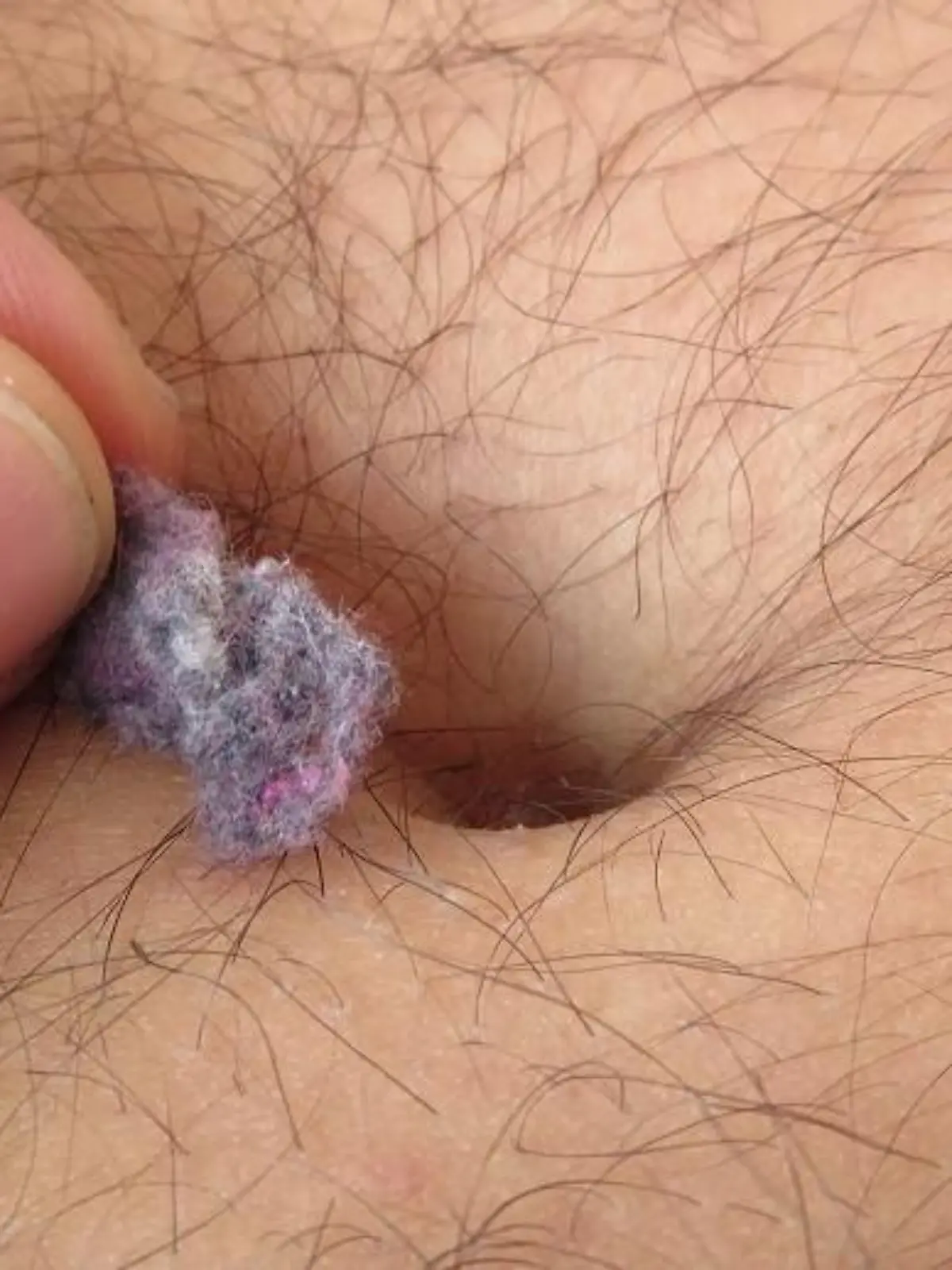 Ein behaarter Mann zieht bunte Fusseln aus seinem Bauchnabel.