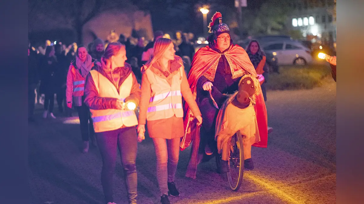 Der Anfang des St. Martin Umzugs in Wesel. Vorne laufen zwei Frauen mit Warnweste voran und rechts ein Mann, der auf einem Drahtesel sitzt. Hinter ihnen befindet sich aufgereiht der Umzug,