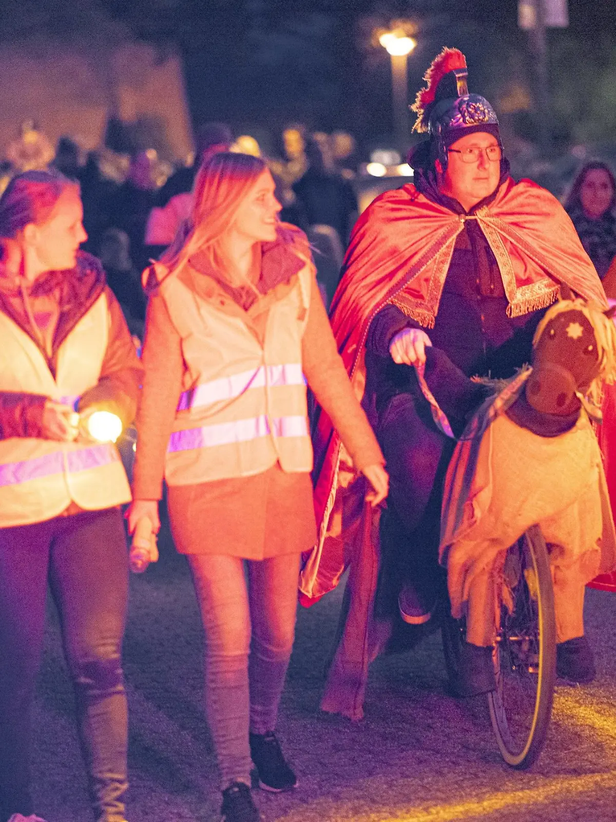 Der Anfang des St. Martin Umzugs in Wesel. Vorne laufen zwei Frauen mit Warnweste voran und rechts ein Mann, der auf einem Drahtesel sitzt. Hinter ihnen befindet sich aufgereiht der Umzug,