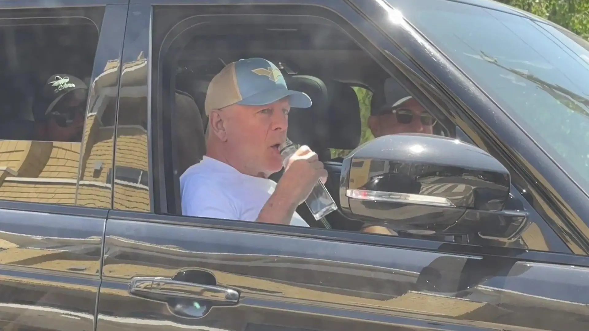 Bruce Willis nimmt auf dem Beifahrersitz eines Autos einen schluck Wasser aus einer Flasche.