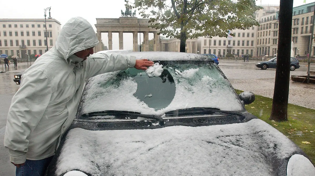 ARCHIV - 13.10.2002, Berlin: Ein Mann befreit am 13.10.2002 die Windschutzscheibe seines am Brandenburger Tor geparkten Autos vom Schnee. Bei Temperaturen von knapp über null Grad ist in Berlin-Brandenburg der erste Schnee gefallen. Der Deutsche Wetterdienst in Potsdam rechnet mit dem kältesten 13. Oktober 2002 seit Beginn der Wetteraufzeichnung. (zu dpa "Sommer im Herbst: Baden unter bunten Bäumen" vom 13.10.2018) Foto: Stephanie Pilick/dpa +++ dpa-Bildfunk +++