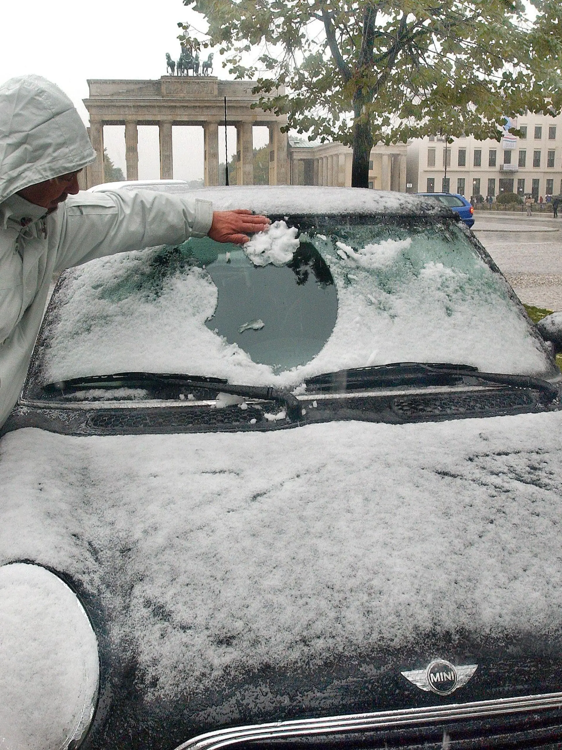 ARCHIV - 13.10.2002, Berlin: Ein Mann befreit am 13.10.2002 die Windschutzscheibe seines am Brandenburger Tor geparkten Autos vom Schnee. Bei Temperaturen von knapp über null Grad ist in Berlin-Brandenburg der erste Schnee gefallen. Der Deutsche Wetterdienst in Potsdam rechnet mit dem kältesten 13. Oktober 2002 seit Beginn der Wetteraufzeichnung. (zu dpa "Sommer im Herbst: Baden unter bunten Bäumen" vom 13.10.2018) Foto: Stephanie Pilick/dpa +++ dpa-Bildfunk +++