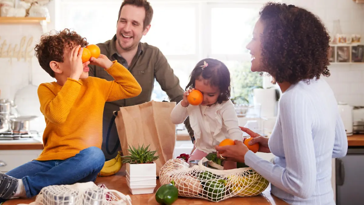 Family Returning Home From Shopping Trip Using Plastic Free Bags Unpacking Groceries In Kitchen