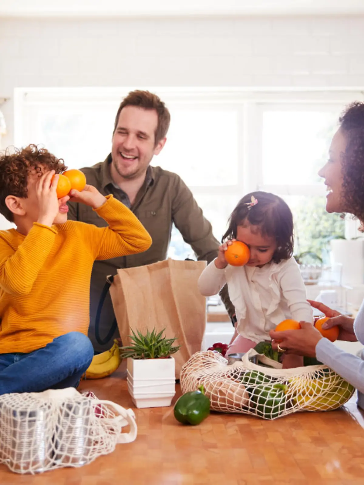 Family Returning Home From Shopping Trip Using Plastic Free Bags Unpacking Groceries In Kitchen