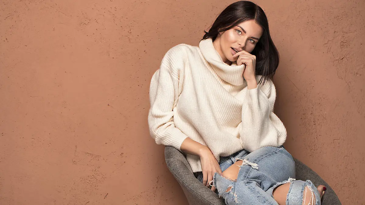 Fashionable beautiful woman in warm sweater posing, looking at camera.