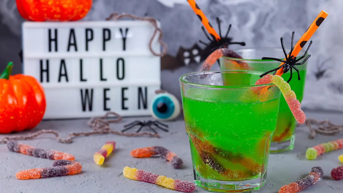 Spooky Halloween cocktail with green bubble drink and candy worms, Halloween decoration with light box on background, horizontal