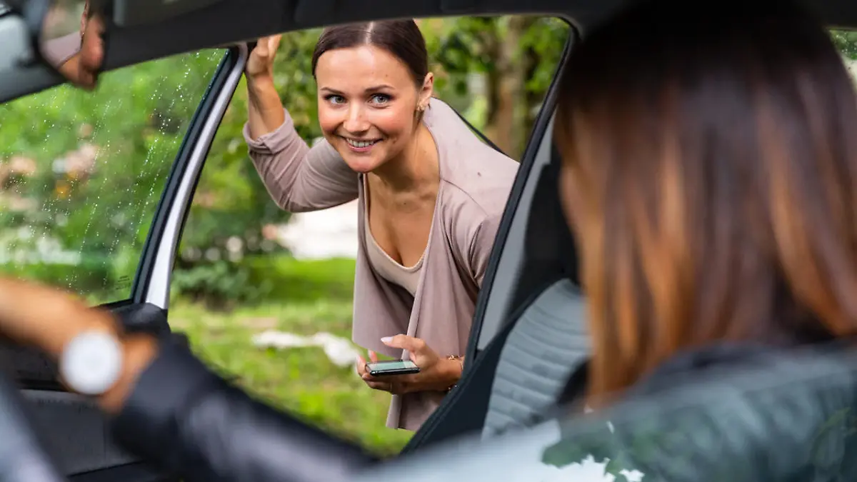 A woman is getting into a car and is looking at the driver.