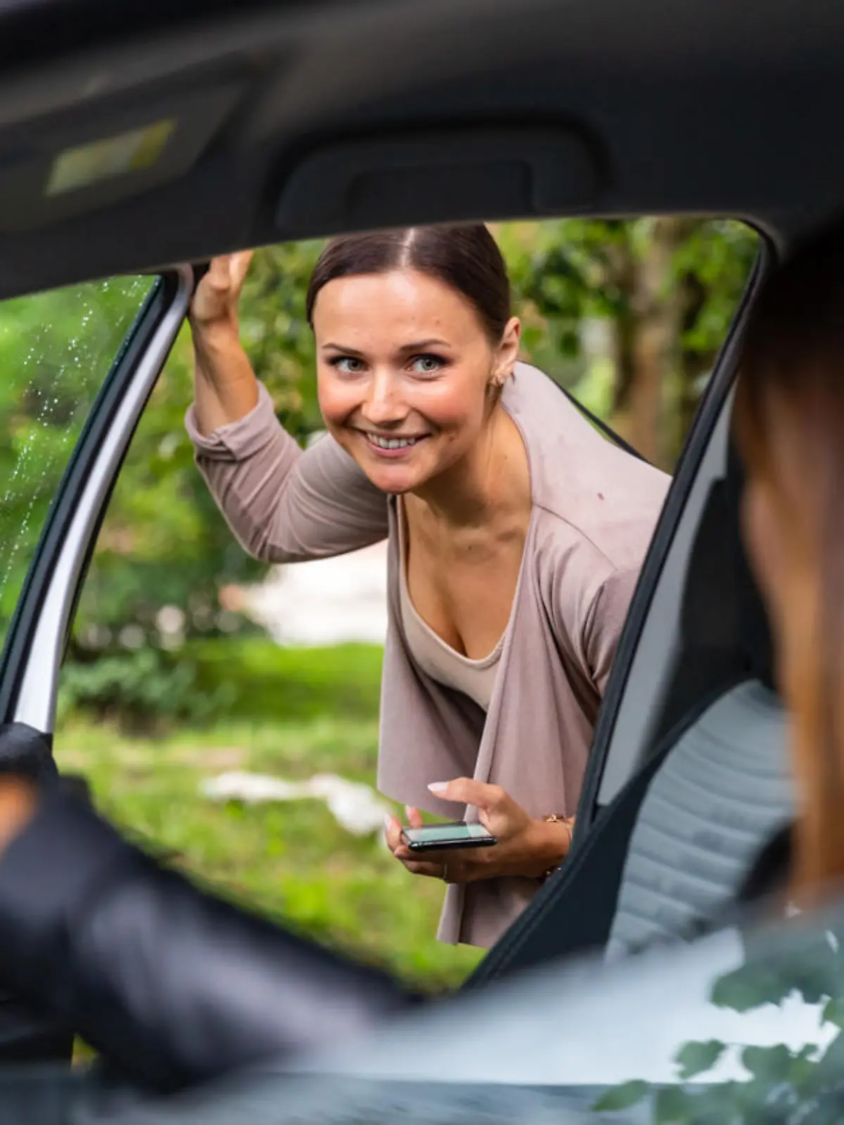 A woman is getting into a car and is looking at the driver.