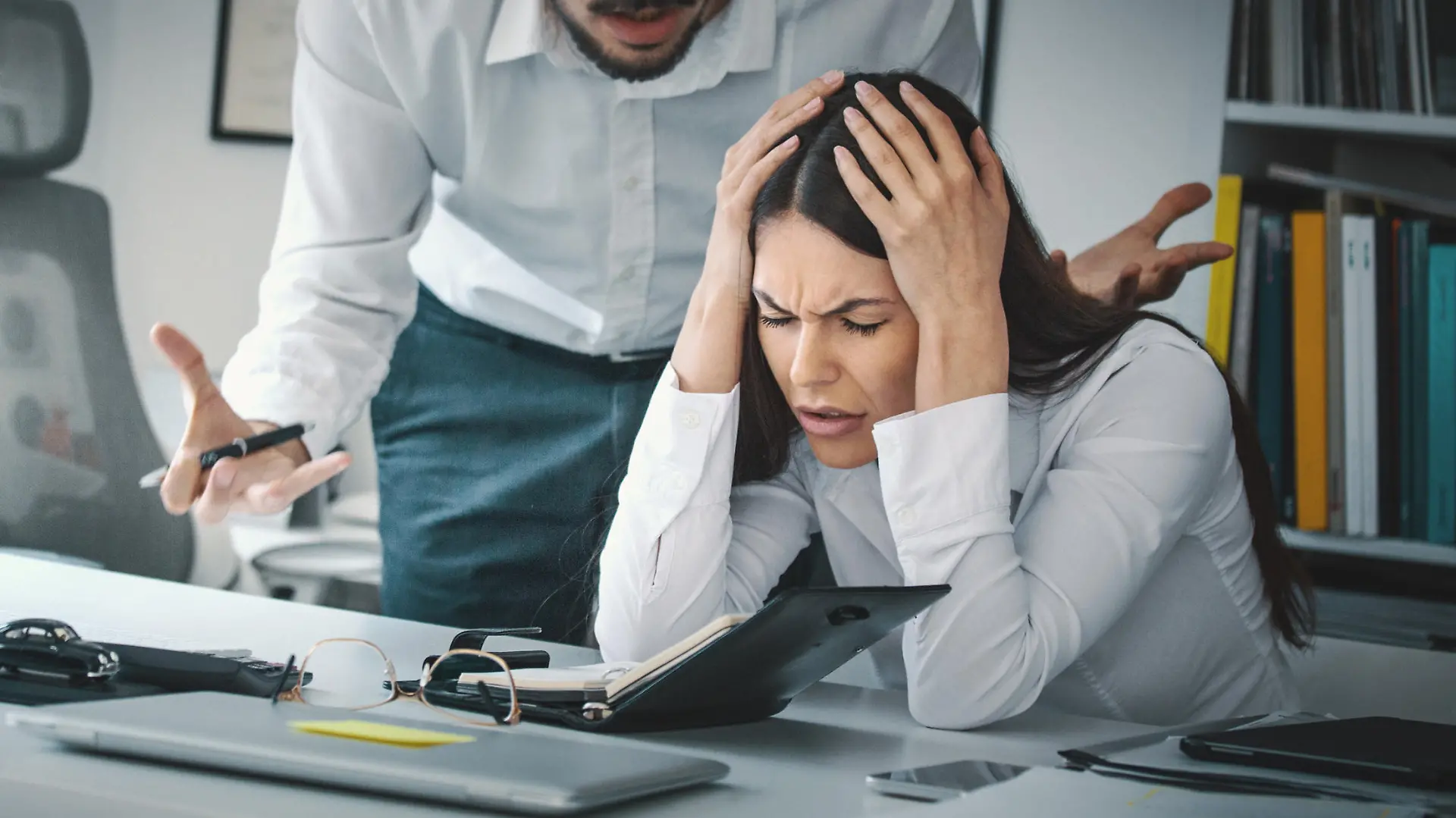 Closeup of late 20's employee at a computer company being criticized by her boss which is giving her a headache.