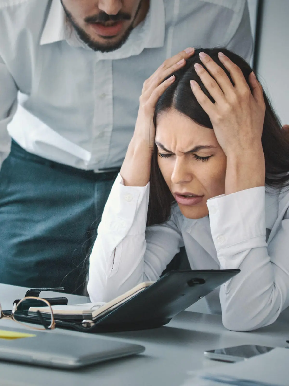 Closeup of late 20's employee at a computer company being criticized by her boss which is giving her a headache.