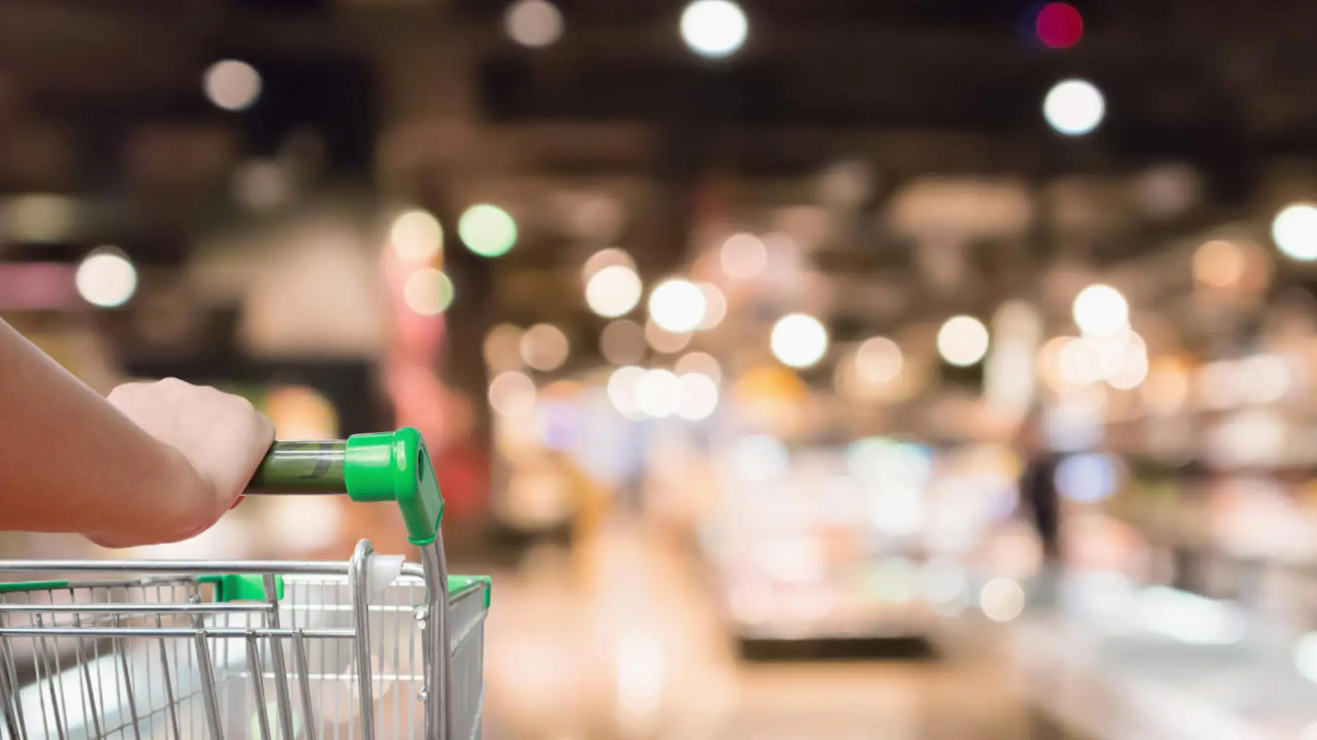 woman hand hold supermarket shopping cart with Abstract grocery store shelves blurred defocused background with bokeh light