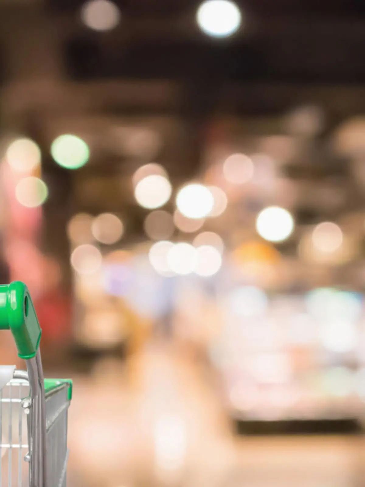 woman hand hold supermarket shopping cart with Abstract grocery store shelves blurred defocused background with bokeh light
