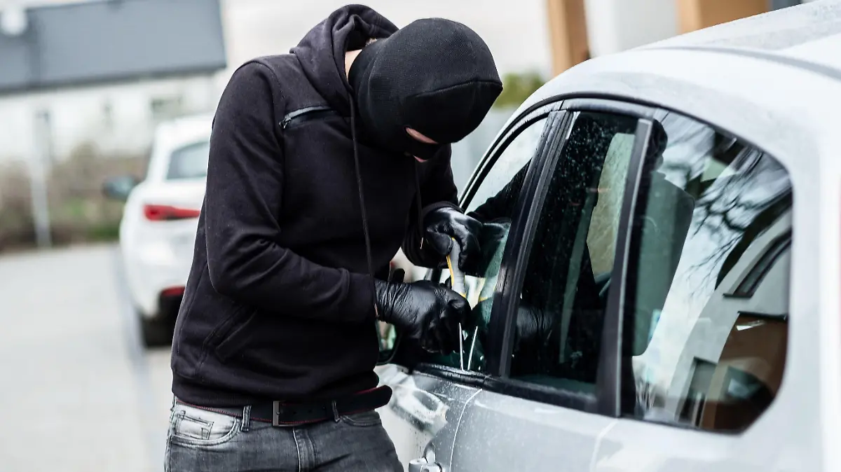 Car thief trying to break into a car with a screwdriver. Car thief, car theft.