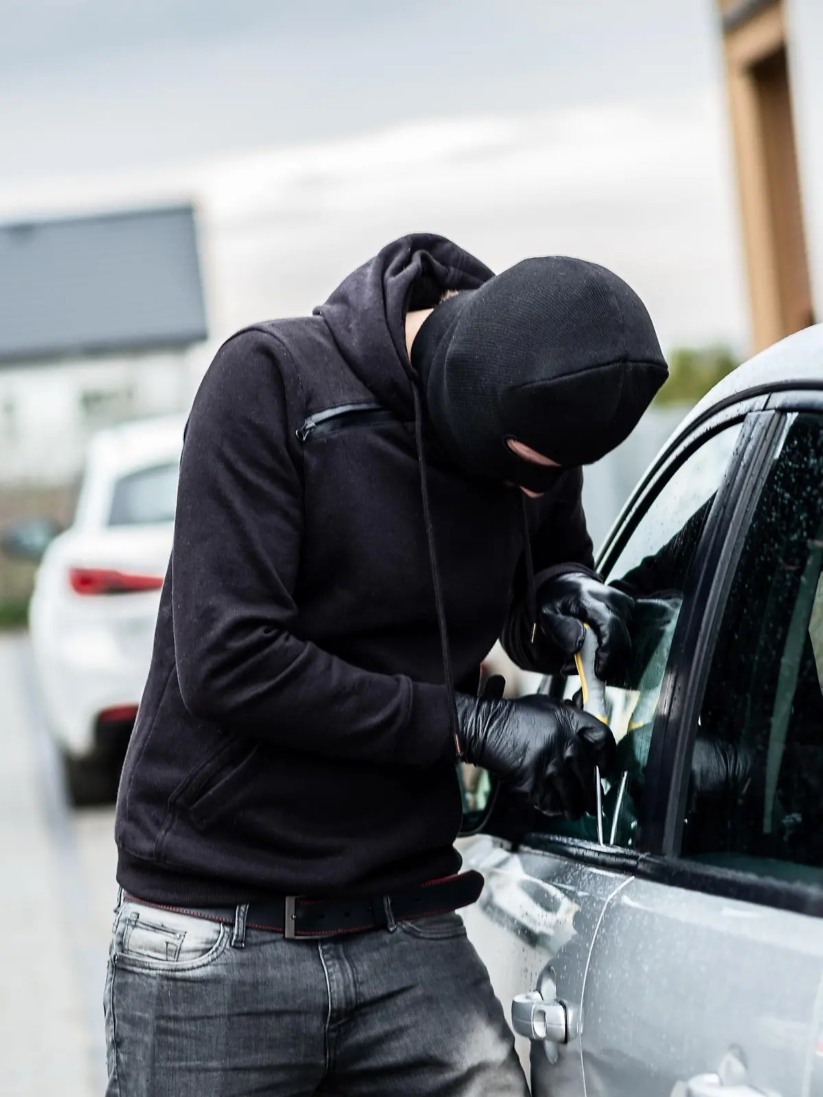 Car thief trying to break into a car with a screwdriver. Car thief, car theft.