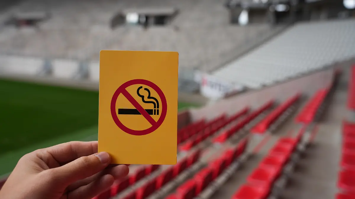 Eine Hand hält eine gelbe Karte mit einer symbolisierten Zigarette, die durchgestrichen ist: Rauchverbot im Stadion des SC Freiburg