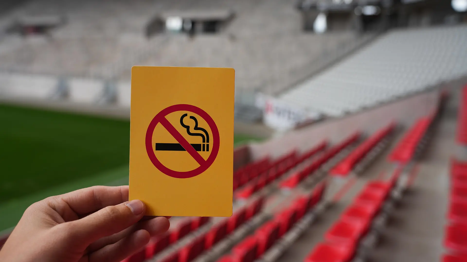 Eine Hand hält eine gelbe Karte mit einer symbolisierten Zigarette, die durchgestrichen ist: Rauchverbot im Stadion des SC Freiburg