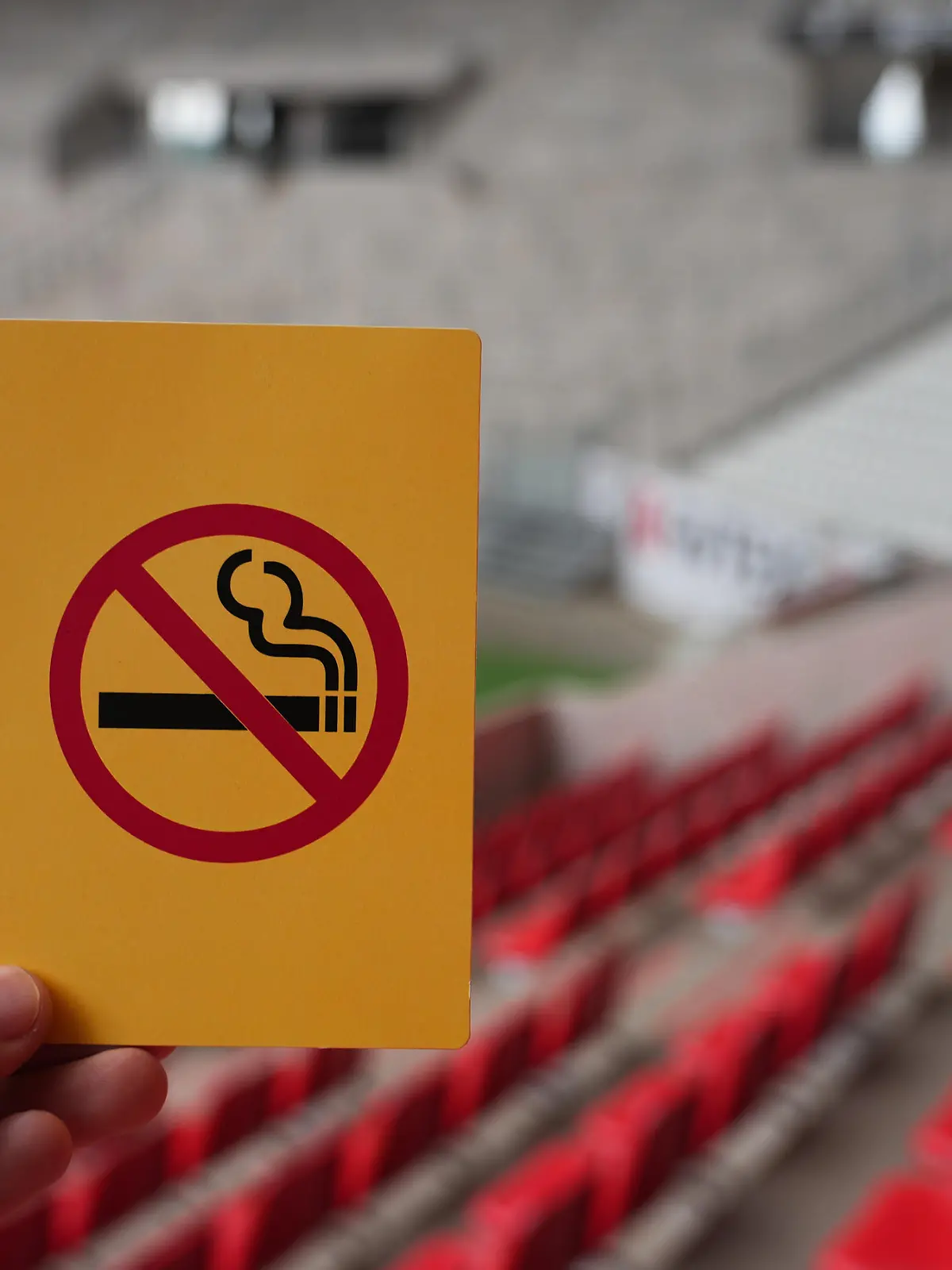 Eine Hand hält eine gelbe Karte mit einer symbolisierten Zigarette, die durchgestrichen ist: Rauchverbot im Stadion des SC Freiburg