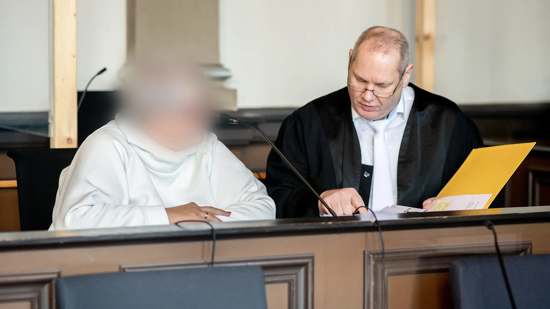 07.11.2022, Niedersachsen, Verden: Die angeklagte Frau sitzt vor Prozessbeginn neben ihrem Anwalt Thorsten Osterkamp in einem Gerichtssaal im Landgericht Verden. Die Hebamme ist wegen Körperverletzung mit Todesfolge angeklagt. Sie betreute im Januar 2015 eine schwangere Frau während einer mehrtägigen Hausgeburt, bei der es zu Komplikationen gekommen ist. Dabei soll die Hebamme erkannt haben, dass es der schwangeren Frau und dem Baby zunehmend schlechter gegangen sei und das Leben des Babys ohne ärztliche Hilfe gefährdet sein könnte. Foto: Hauke-Christian Dittrich/dpa - ACHTUNG: Person(en) wurde(n) aus rechtlichen Gründen gepixelt +++ dpa-Bildfunk +++