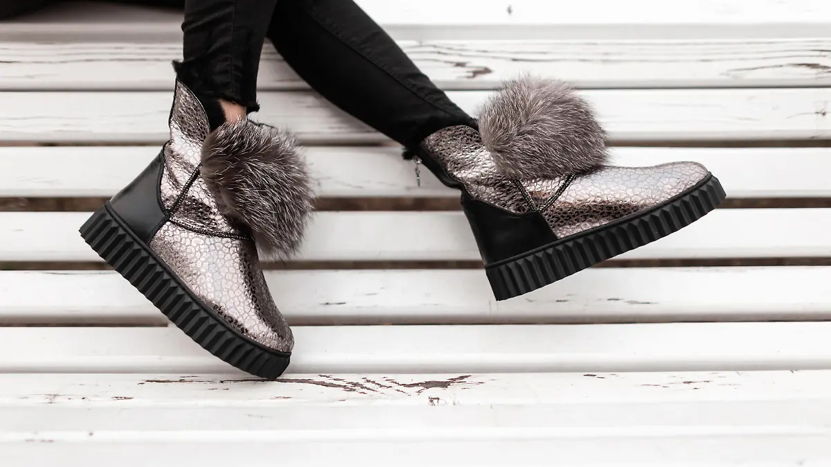 Beautiful silver shiny winter shoes with gray fur on female legs. New collection of fashionable warm glamorous boots. Modern design. Seasonal fashion. Close-up.