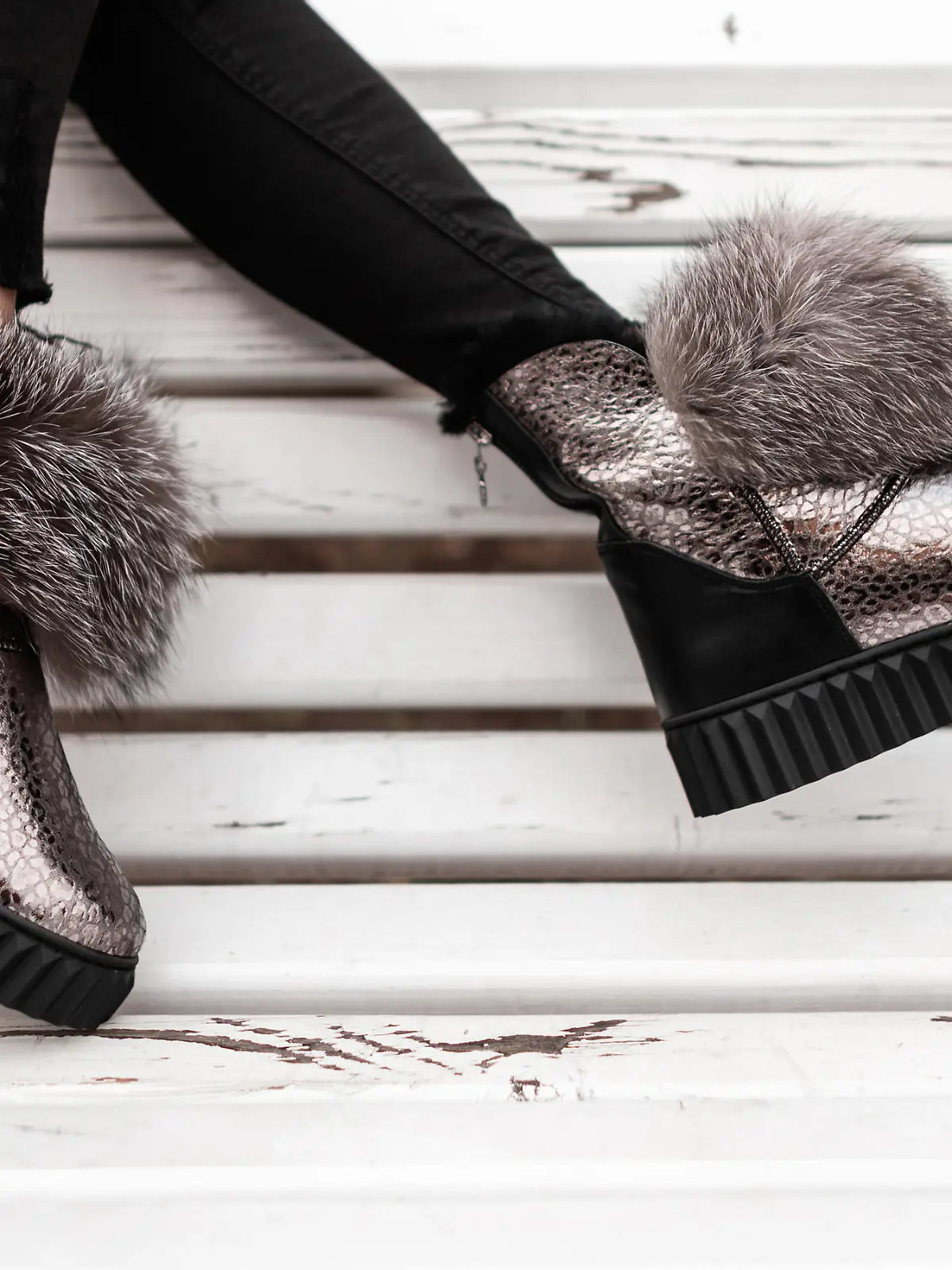 Beautiful silver shiny winter shoes with gray fur on female legs. New collection of fashionable warm glamorous boots. Modern design. Seasonal fashion. Close-up.