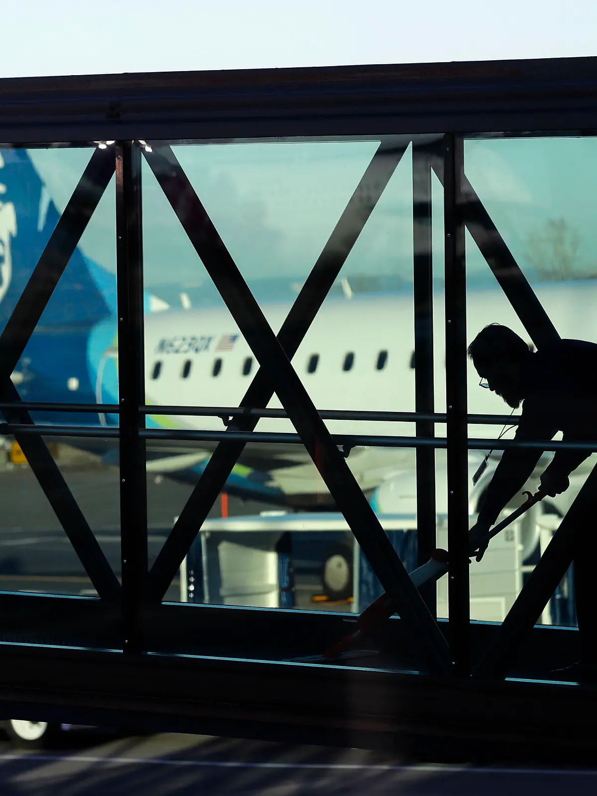 FILE - A worker cleans a jet bridge at Paine Field in Everett, Wash., before passengers board an Alaska Airlines flight on March 4, 2019. Seattle-based Alaska Airlines owns Horizon Air. An off-duty pilot riding in the extra seat in the cockpit of a Horizon Air passenger jet on Sunday, Oct. 22, 2023, tried to shut down the engines in mid-flight and had to be subdued by the crew, according to a pilot flying the plane. (AP Photo/Ted S. Warren, File)