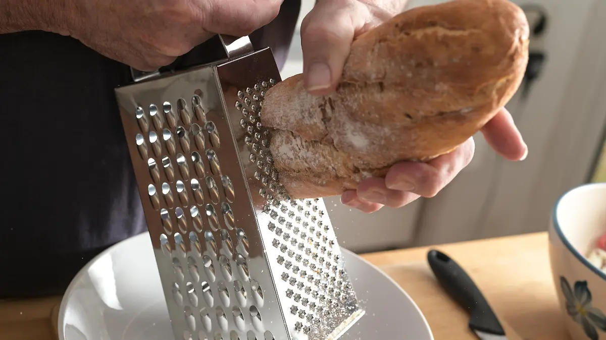 Hands of a man are grating hard bread on a grater to get breadcrumbs, selected focus, little motion blur