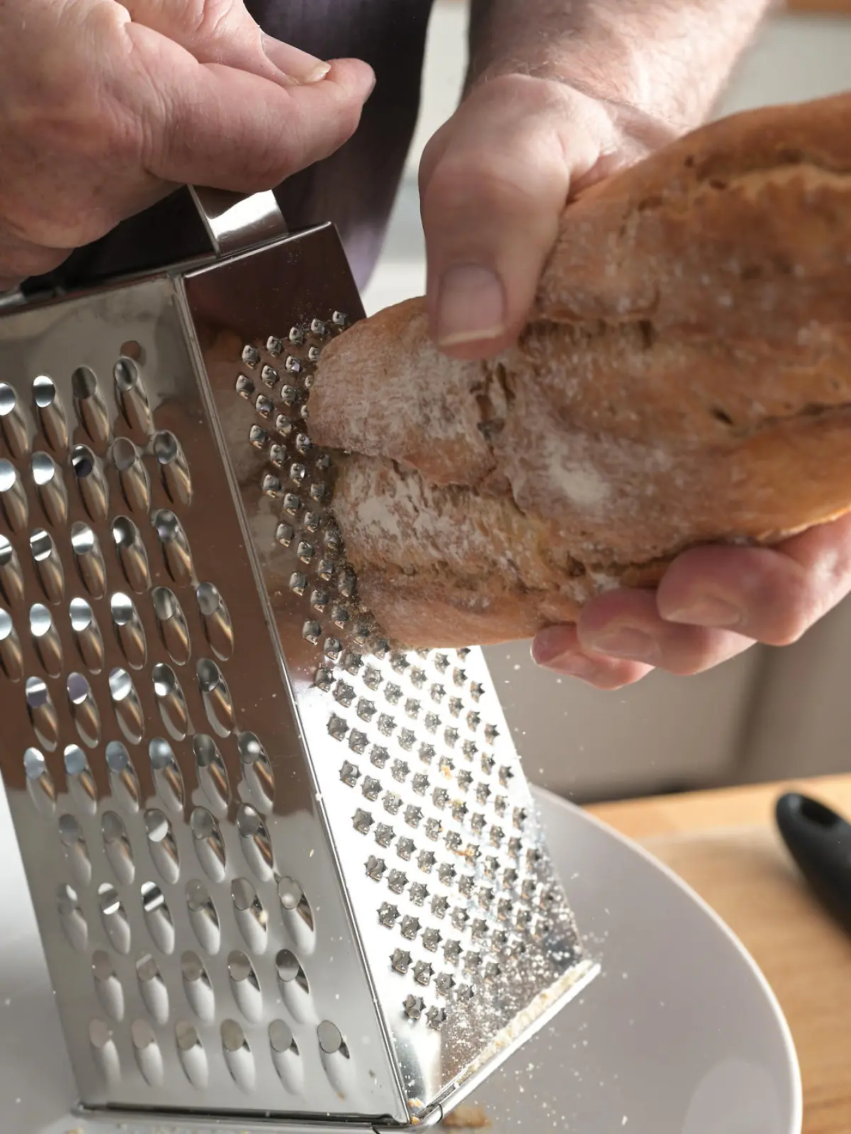 Hands of a man are grating hard bread on a grater to get breadcrumbs, selected focus, little motion blur