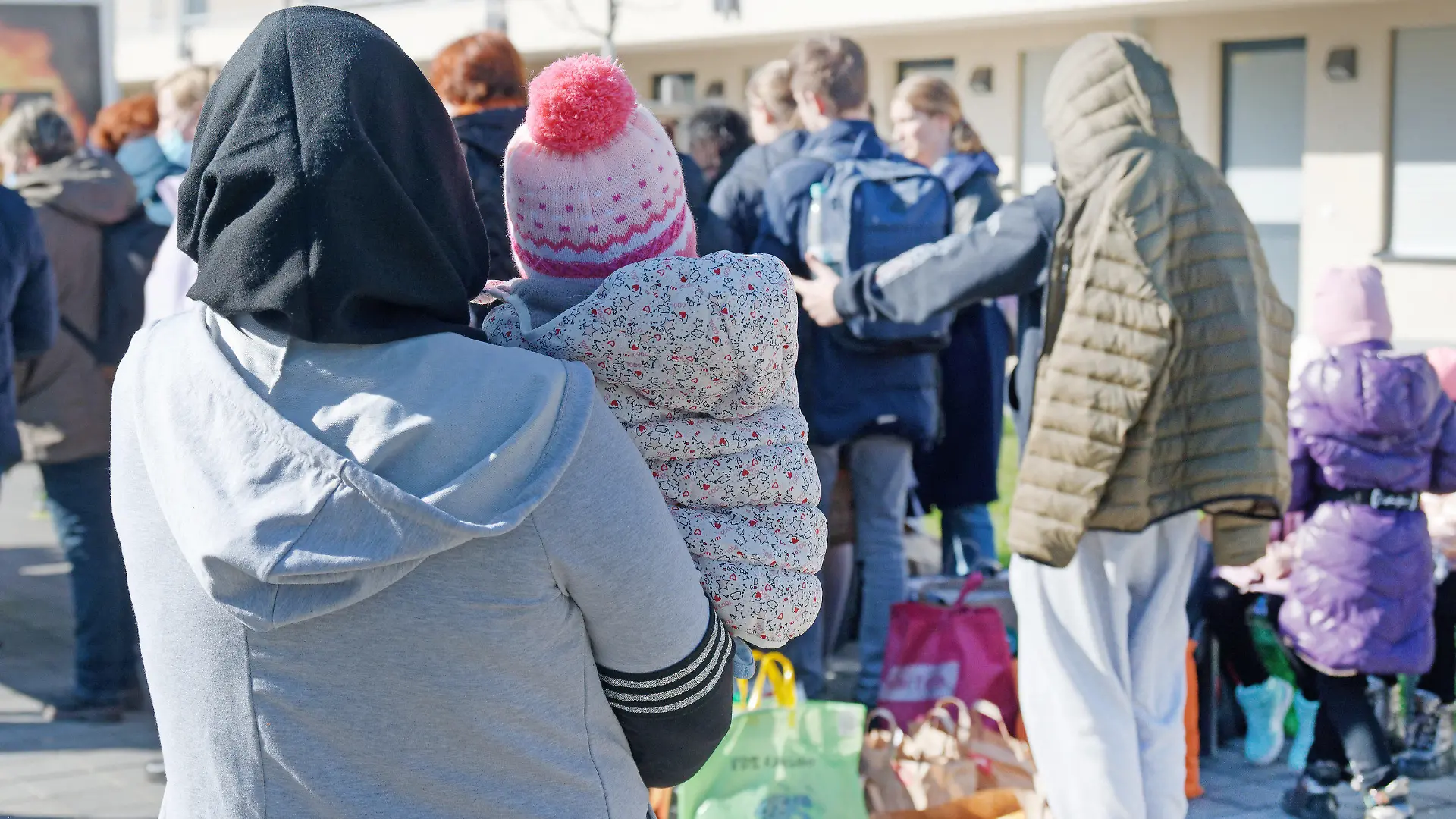 ARCHIV - 03.03.2022, Nordrhein-Westfalen, Köln: Geflüchtete aus der Ukraine stehen vor den Gebäuden einer Flüchtlingsunterkunft. Nordrhein-Westfalen plant derzeit nicht, Bezahlkarten einzuführen, um Bargeld-Leistungen für Asylbewerber zu ersetzen.     (zu dpa «NRW plant keine Bezahlkarten für Flüchtlinge: "Persönlichkeitsrechte"»). Foto: Henning Kaiser/dpa +++ dpa-Bildfunk +++