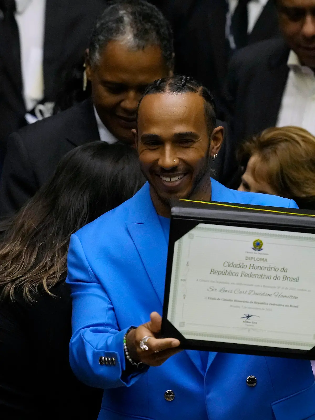 07.11.2022, Brasilien, Brasilia: Lewis Hamilton (M), Rennfahrer aus Großbritannien, präsentiert seinen Titel als Ehrenbürger Brasiliens. Nach seinem Sieg in Interlagos in der Vorsaison feierte Hamilton mit einer brasilianischen Fahne auf dem Podium, was den Kongressabgeordneten Figueiredo dazu veranlasste ihn als Ehrenbürger vorzuschlagen. Foto: Eraldo Peres/AP/dpa +++ dpa-Bildfunk +++