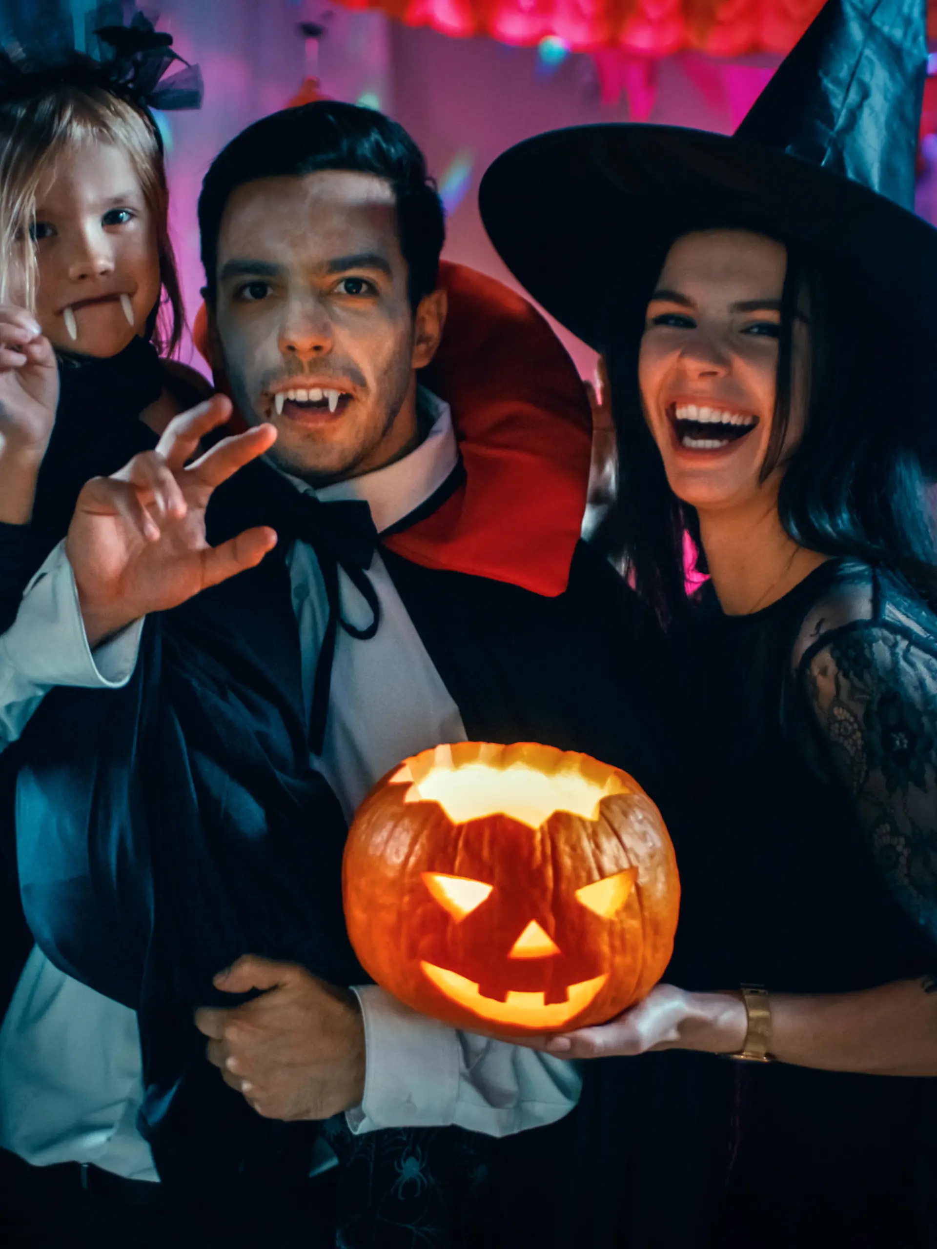 Halloween Costume Party: Father Count Dracula Holds Little Bat Girl Daughter and Hugs Witch Wife for a Happy Family Portrait. In the Background Monsters Having Fun