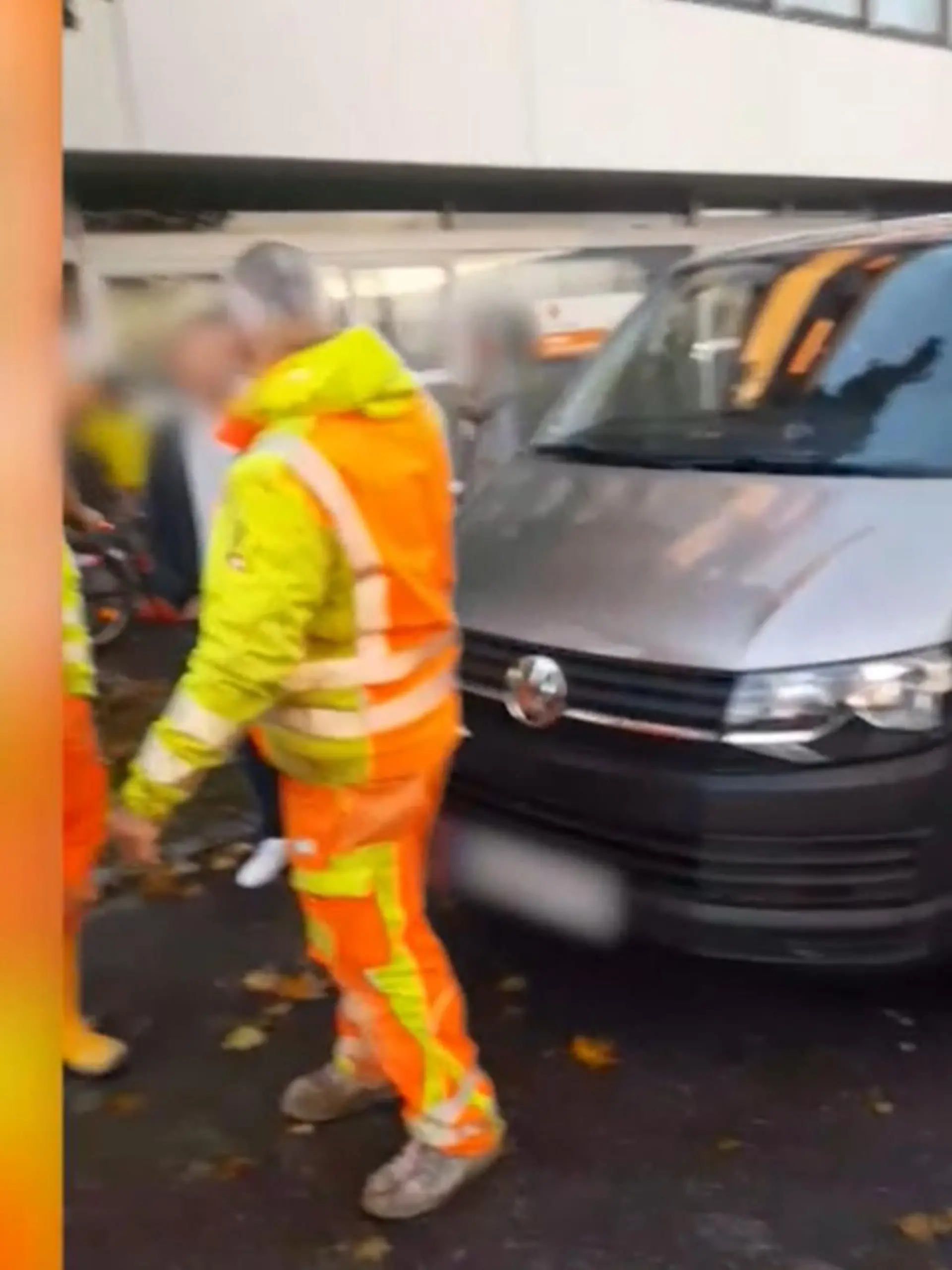 Ein grauer VW-Bus, davor stehen Bauarbeiter in Arbeitskleidung