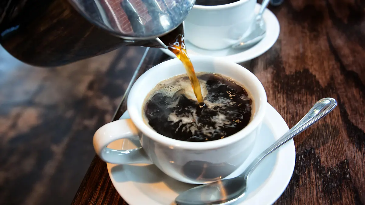 Fresh hot coffee being poured into a cup from a stainless steel french press in a trendy cafe