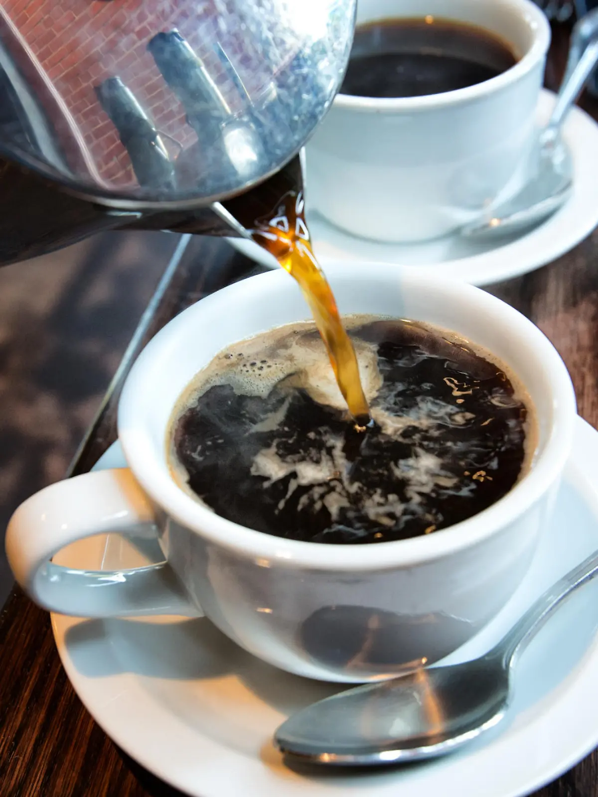 Fresh hot coffee being poured into a cup from a stainless steel french press in a trendy cafe