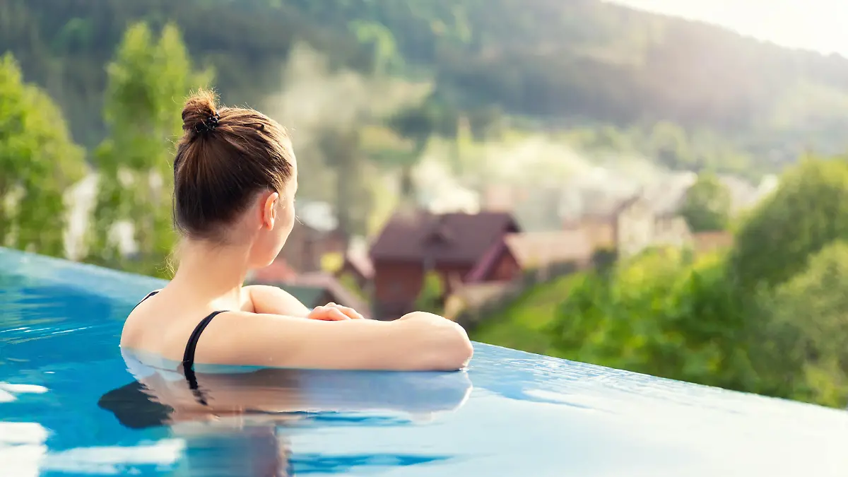 Frau, die in einem Pool mit Aussicht auf eine Berglandschaft entspannt.