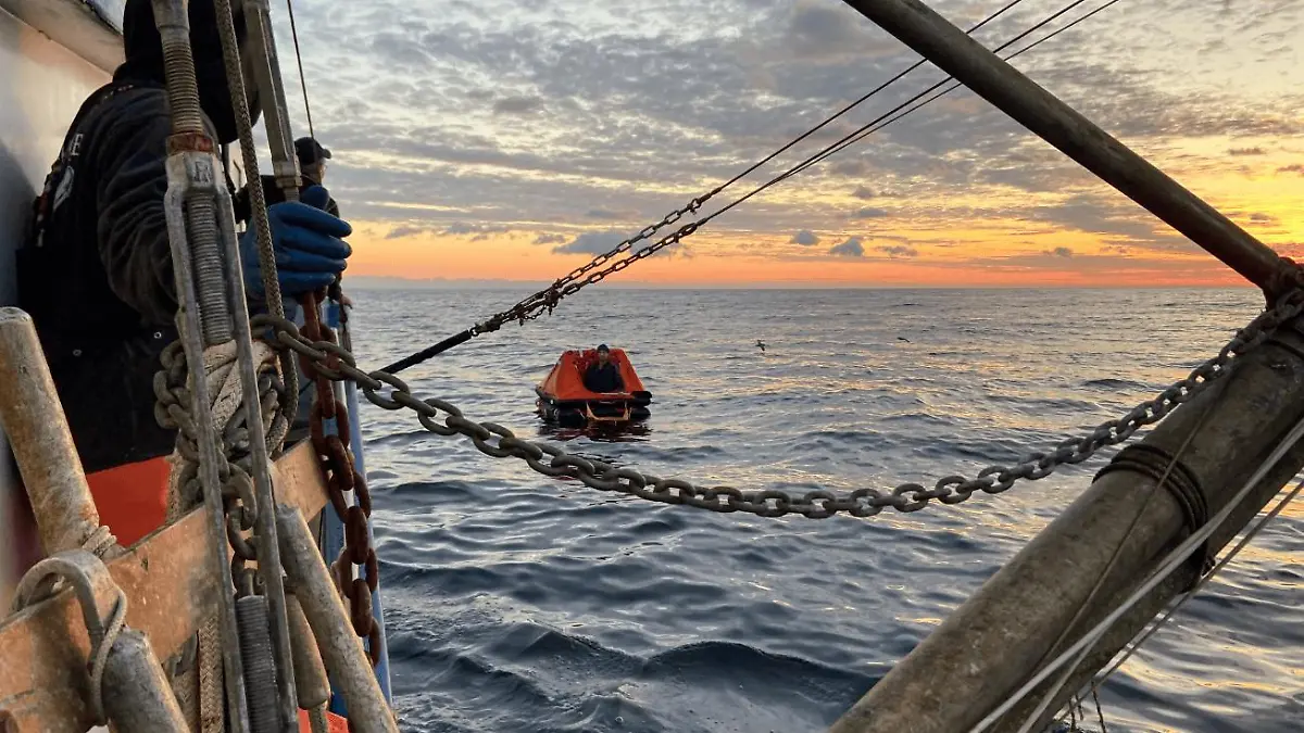Eine Rettungsinsel treibt im Meer, ein Boot steuert darauf zu.