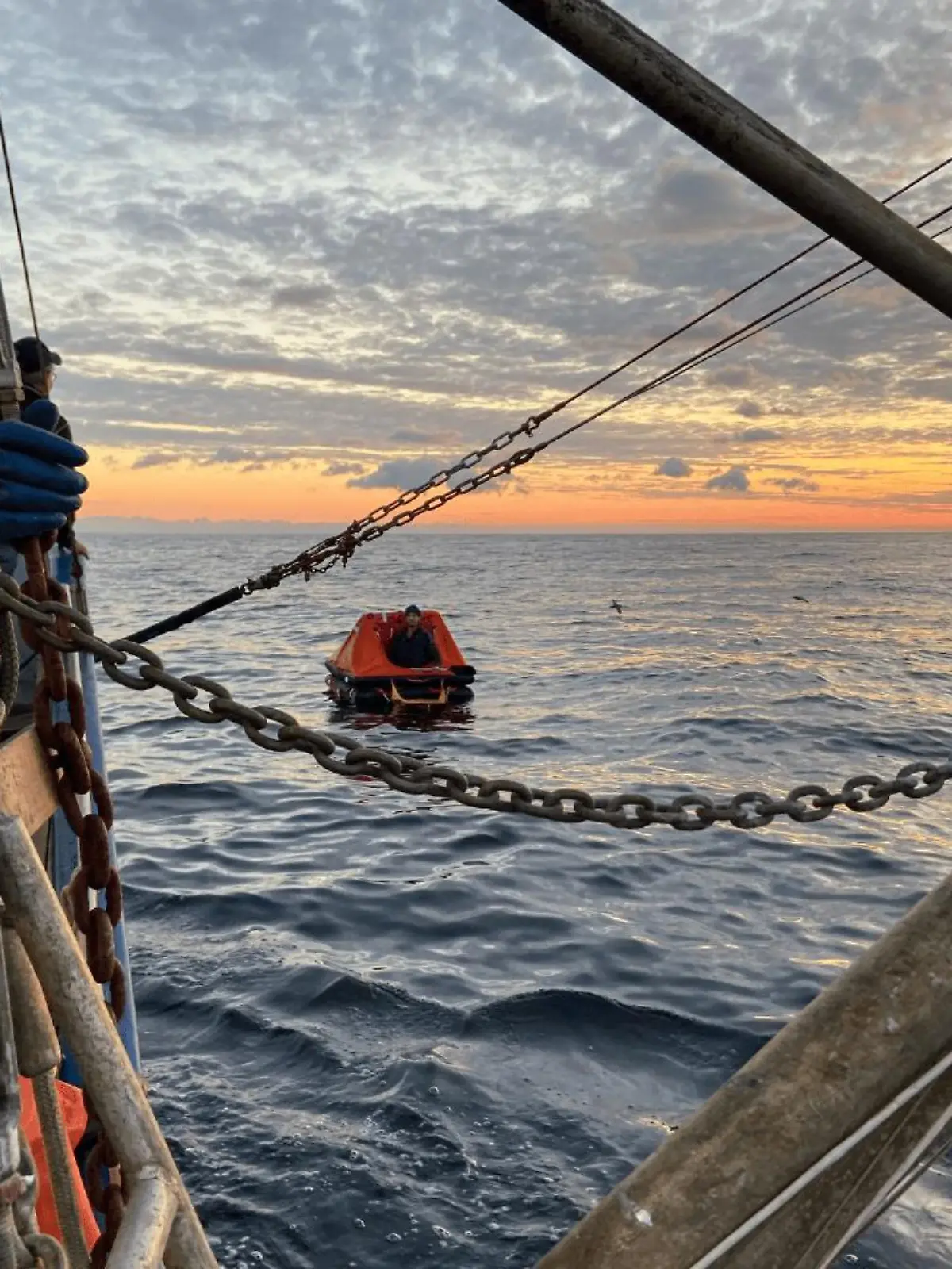 Eine Rettungsinsel treibt im Meer, ein Boot steuert darauf zu.