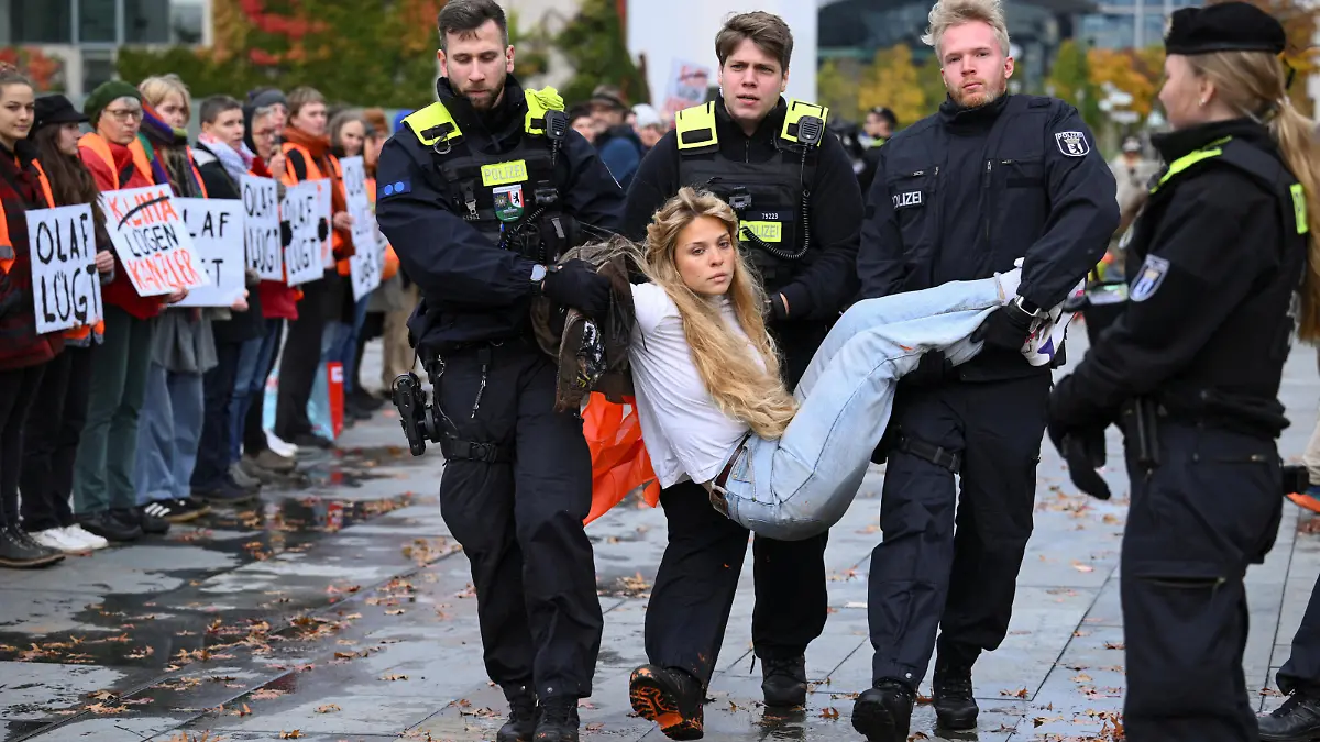 Police officers detain an activist while activists of the 'Letzte Generation' (Last Generation) stand with posters lettering 'Olaf is lying' to protest in front of the Chancellery in Berlin, Germany October 31, 2023. REUTERS/Annegret Hilse