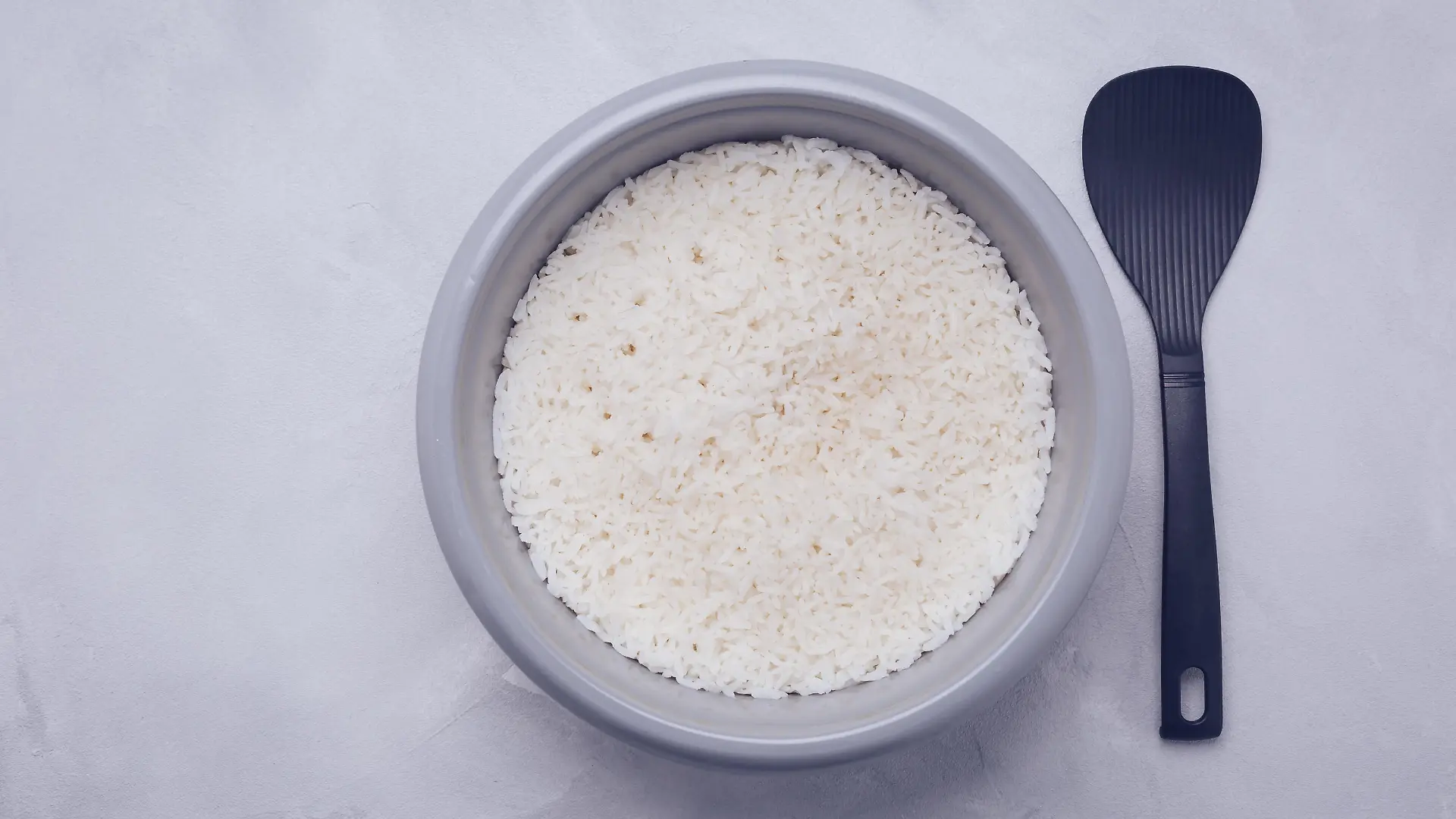 Rice in rice cooker or steamer with spoon, top view