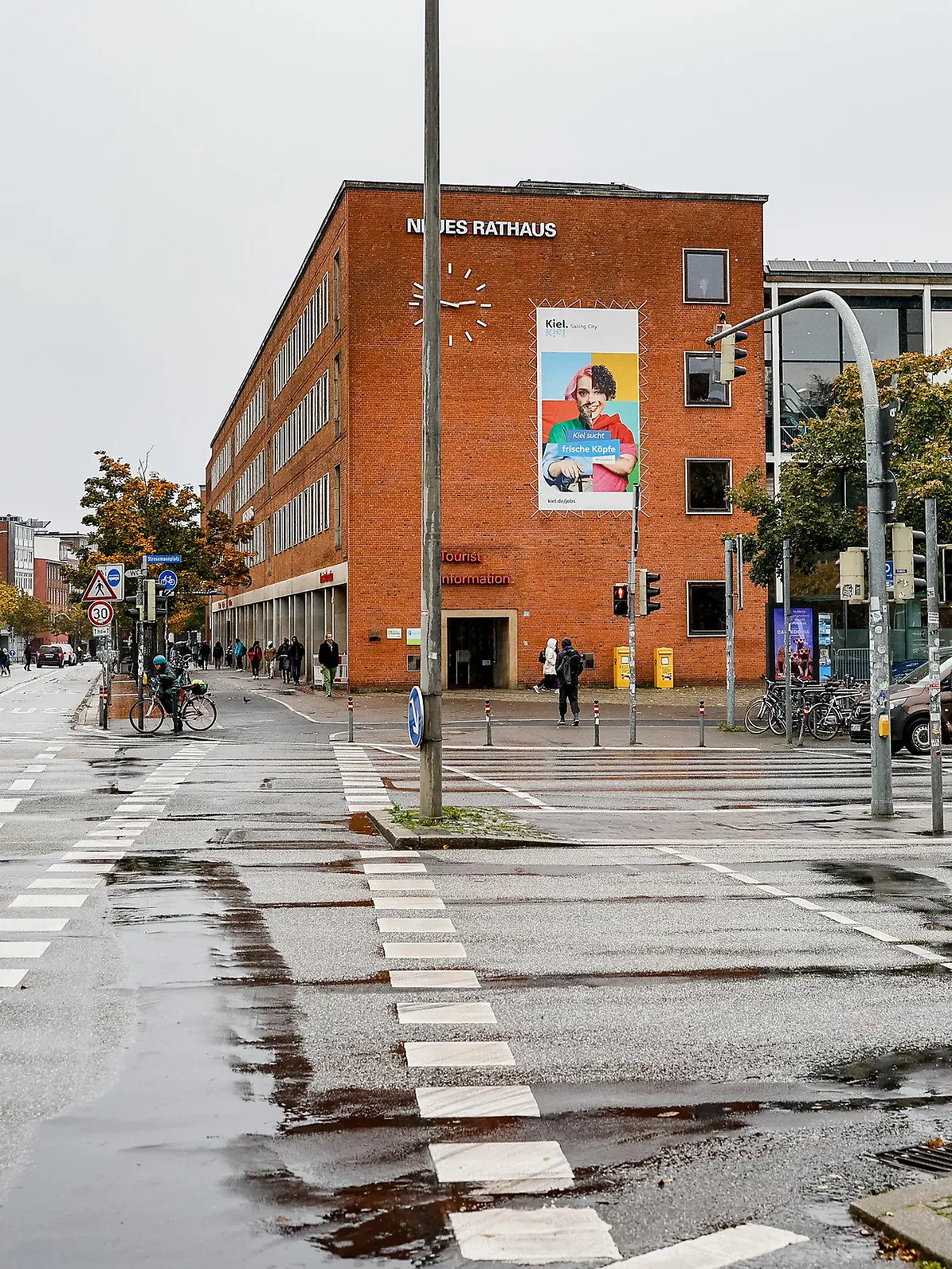 19.10.2023, Schleswig-Holstein, Kiel: Regenpfützen sammeln sich auf der Kreuzung vor dem Neuen Kieler Rathaus auf der sich ein schwerer Unfall ereignet hat. Die dabei tödlich verletzte Frau hatte nach neuen Erkenntnissen schon vorher schwere Verletzungen erlitten. Die Polizei ermittelt deshalb wegen eines Tötungsdeliktes, wie sie am Donnerstag in Kiel mitteilte. Foto: Axel Heimken/dpa +++ dpa-Bildfunk +++